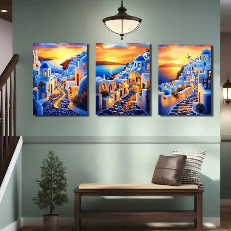 Three-panel artwork of a sunset over a coastal village with blue domes, displayed on a wall above a bench.