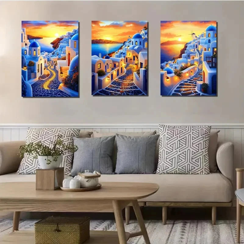 Three framed artworks of a sunset over a coastal village on a wall above a sofa.