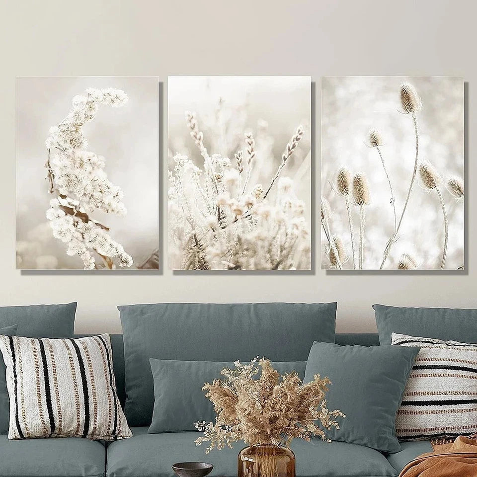 Three framed artworks of floral arrangements on a wall above a sofa with decorative pillows.