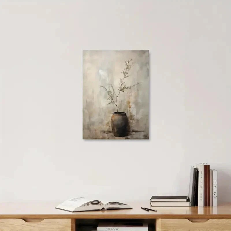 Framed artwork of a vase with branches on a wall above a shelf with books and an open book.