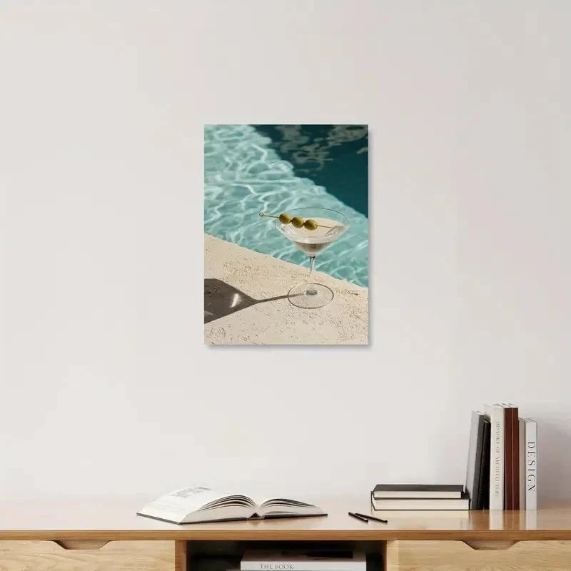 Framed artwork of a martini glass by a pool on a shelf with books.